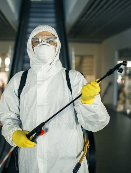 A man in a sanitizing disifection suit holding spray near the escalator to remove potential health risks