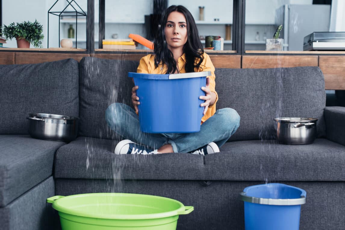 Woman holding bucket on sofa during HOA water damage